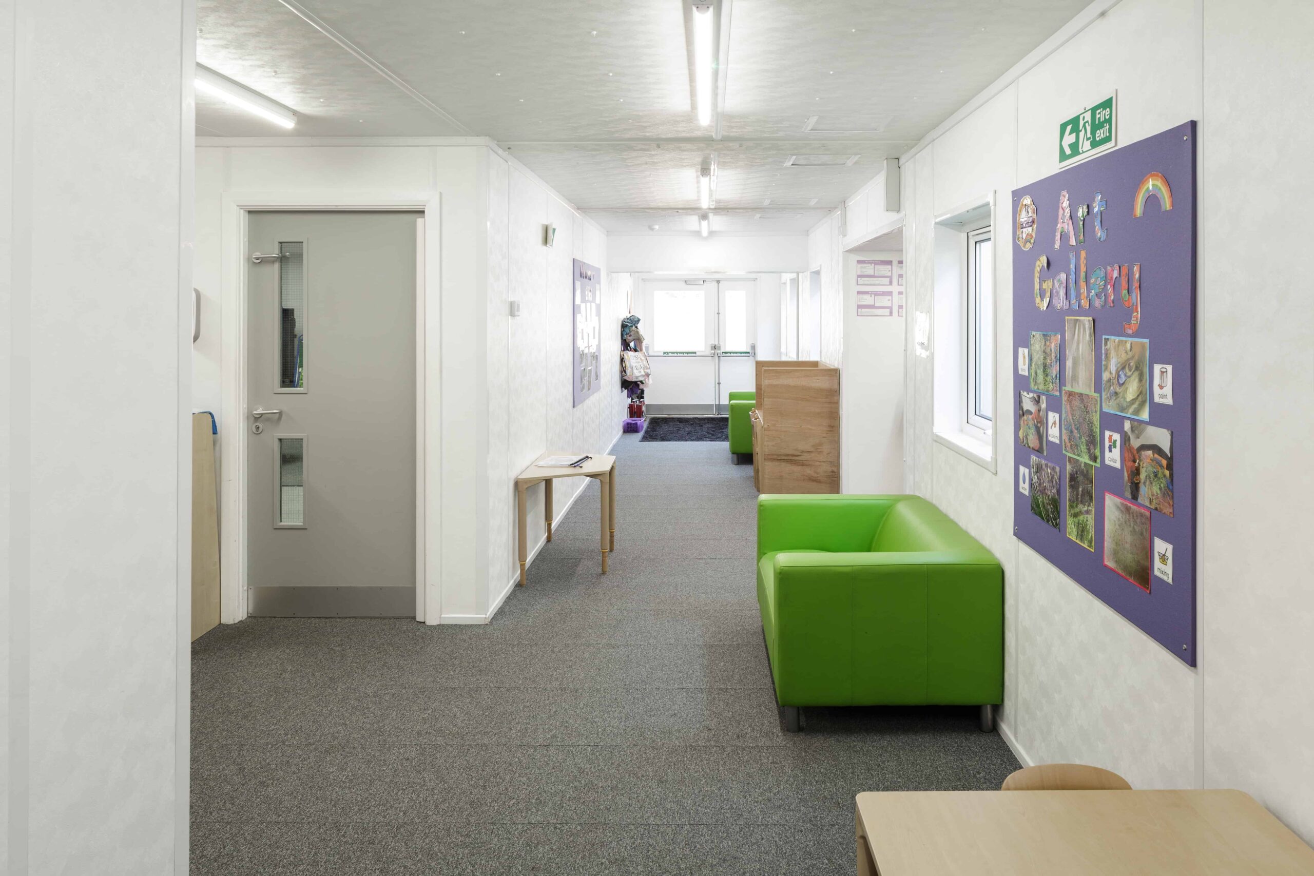 Inside temporary school building, green couch with an art gallery board hung up. Learning space outside the classroom.