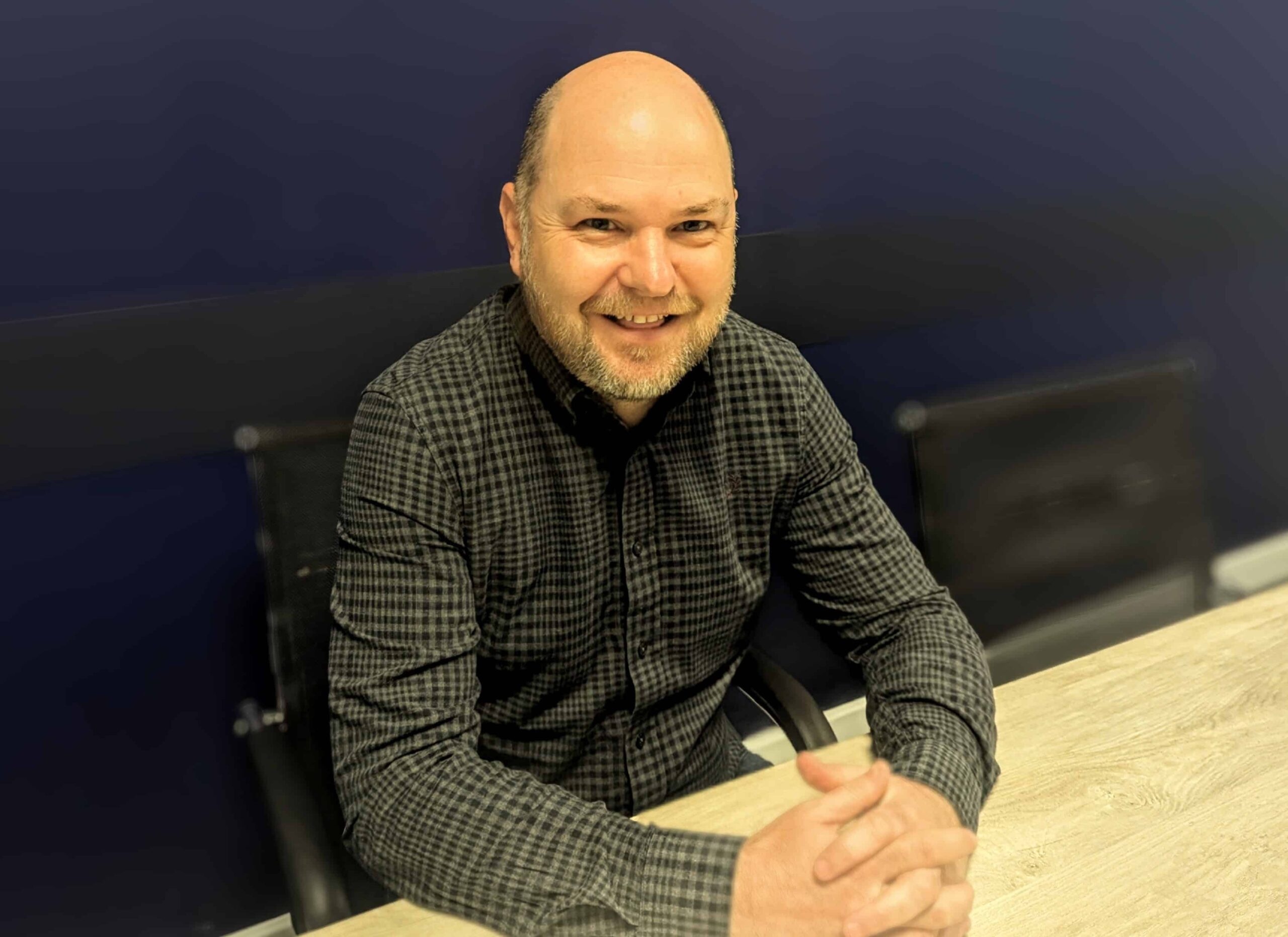 Head of Pre-Construction, Richard Hook. Bald man wearing a long sleeve shirt, sat at a desk. 